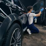 Man in repair workshop washing car window during car valeting